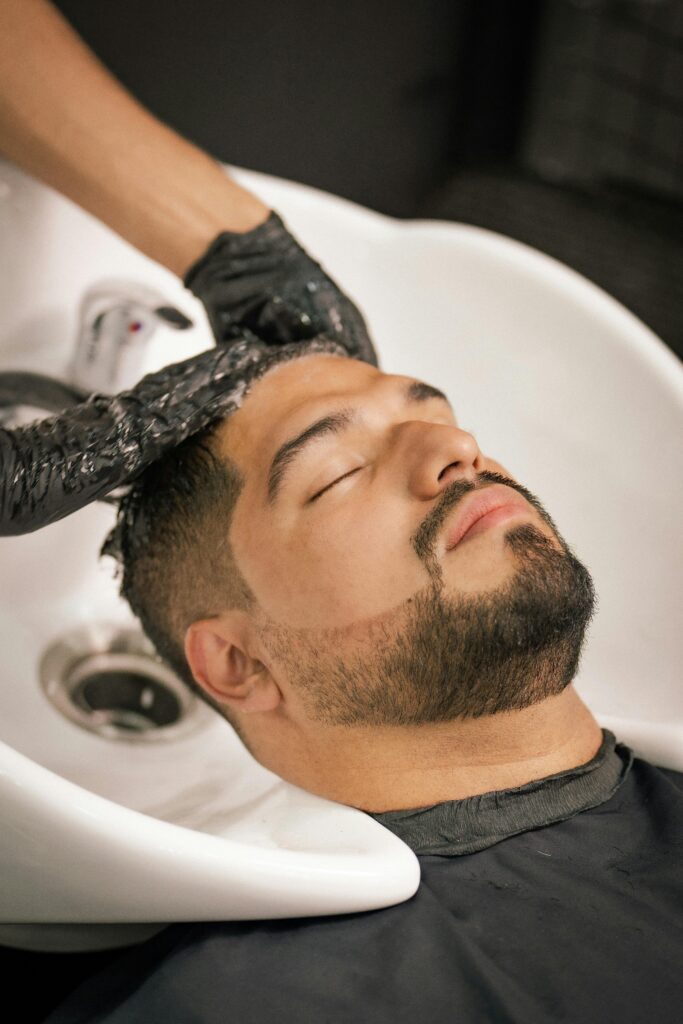 pexels-photo-19762215-19762215 A man with closed eyes enjoys a calming hair wash at a barbershop sink.