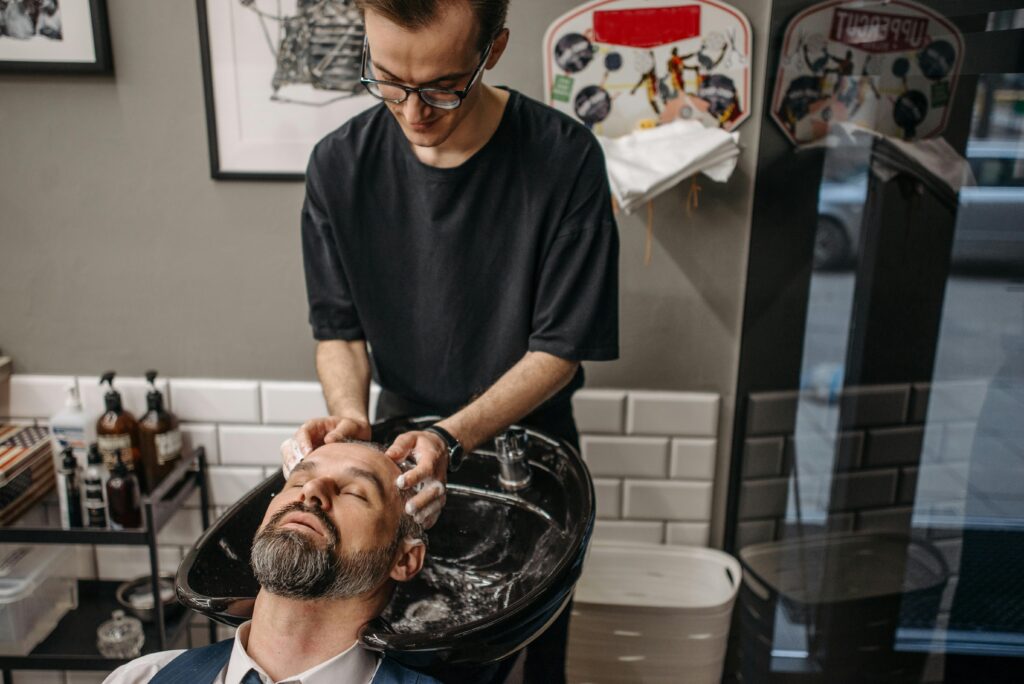 pexels-photo-7518730-7518730 Barber washing client's hair at shampoo station in modern salon setting.